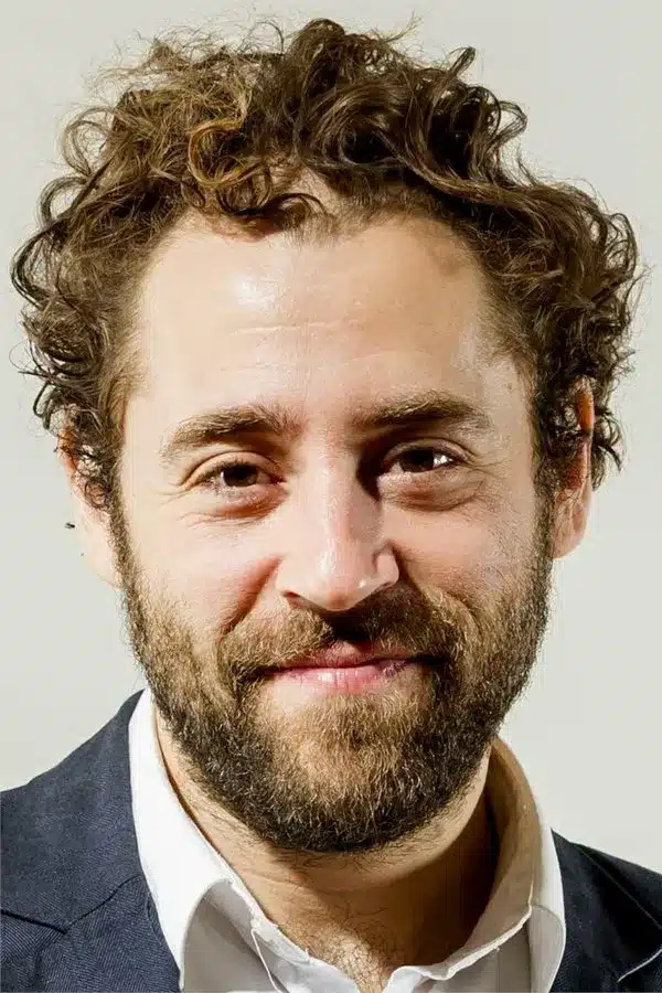 Michael Rubenfeld Michael Rubenfeld smiling in a close-up portrait with curly hair and a beard.
