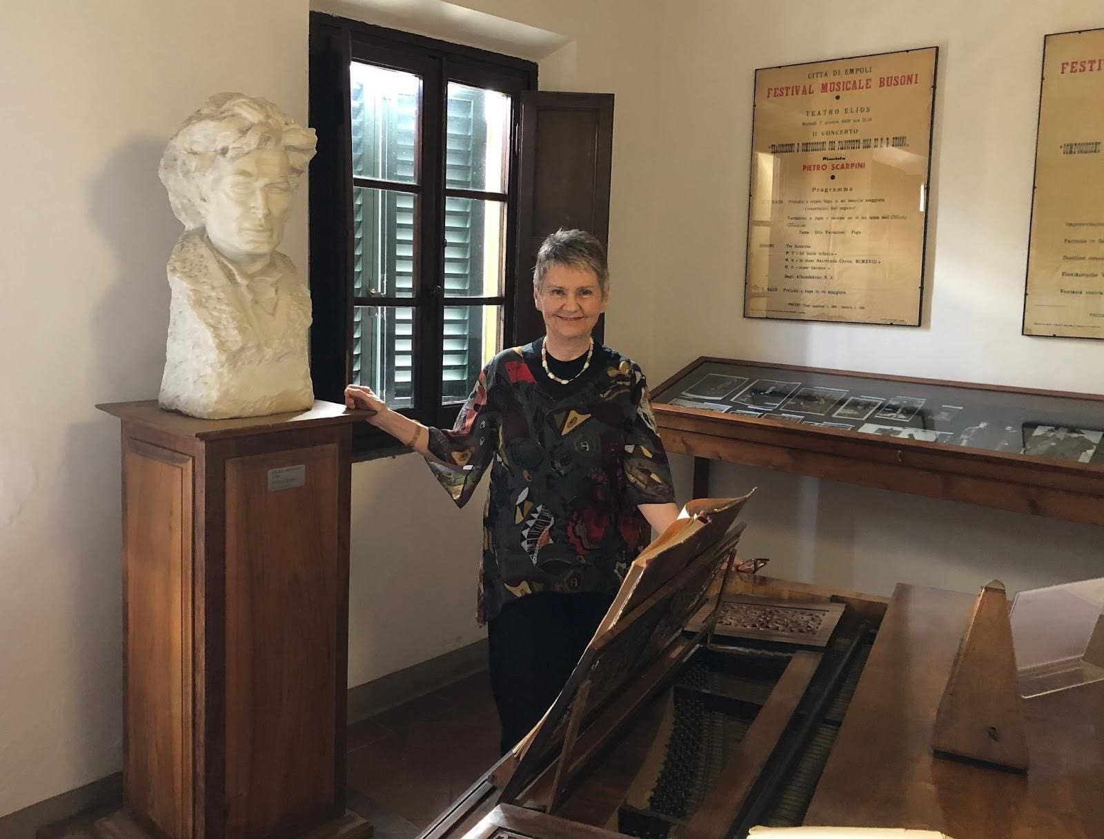 Aloma Bardi Aloma Bardi standing beside a bust and piano in a music exhibition room.