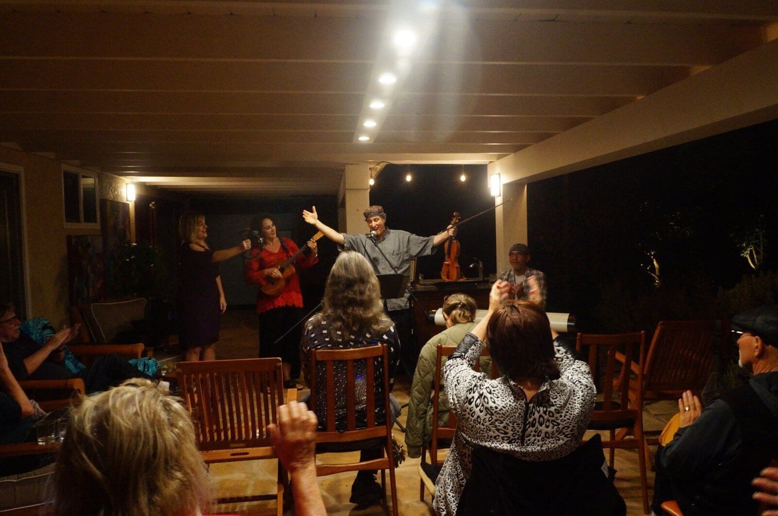 Musical performance on a patio with musicians and audience clapping.
