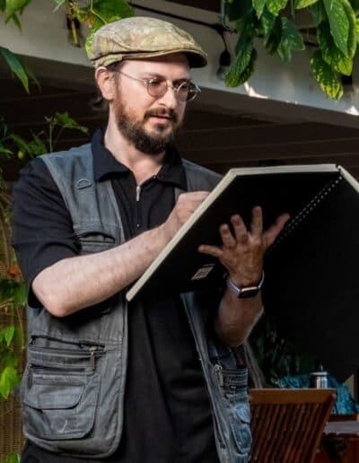 Oleg Tsank sketching outdoors with a notebook, surrounded by greenery at Yiddishland California.